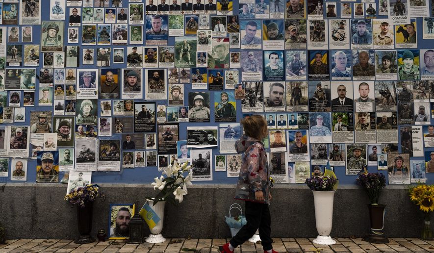 A girl looks at the phots of Ukrainian soldiers killed in the county's war against Russia, at the Wall of Remembrance in Kyiv, Ukraine, Thursday, July 27, 2023. (AP Photo/Jae C. Hong)