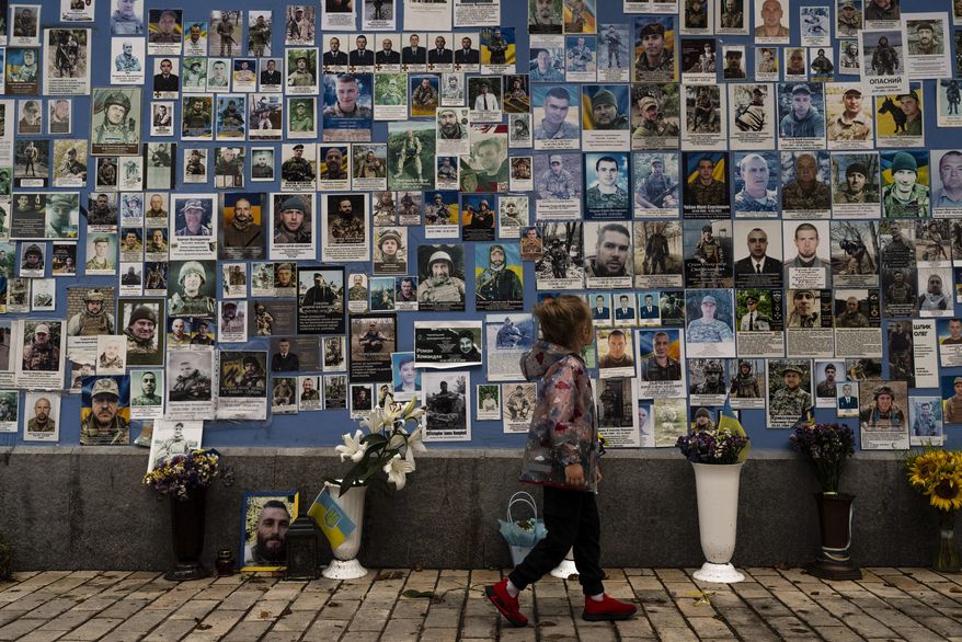 A girl looks at the phots of Ukrainian soldiers killed in the county's war against Russia, at the Wall of Remembrance in Kyiv, Ukraine, Thursday, July 27, 2023. (AP Photo/Jae C. Hong)
