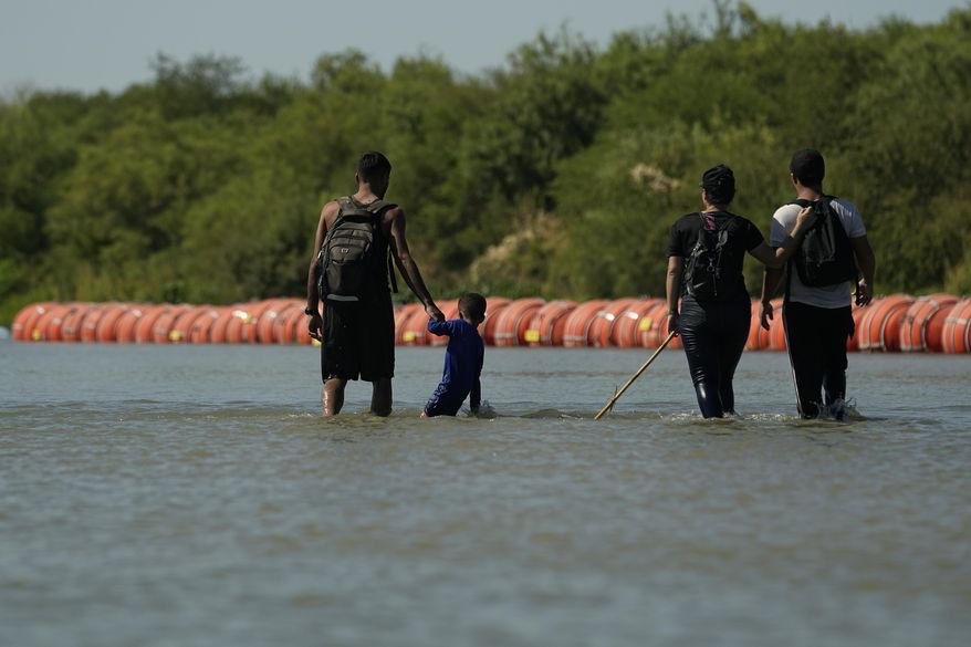 Migrants crossing into the U.S. from Mexico walk along large buoys being used as a floating border barrier on the Rio Grande Tuesday, Aug. 1, 2023, in Eagle Pass, Texas. (AP Photo/Eric Gay)