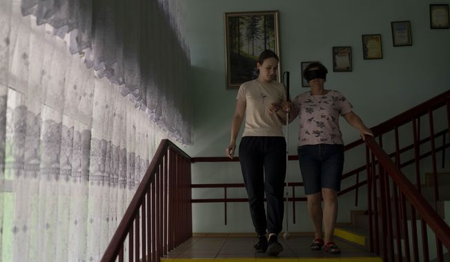 Vlada Ryabets, left, helps blindfolded Tatiana Zhylchenko walk down the steps during an exercise designed to help partners living with soldiers blinded in the war better understand what the veterans experience, at a rehabilitation center near Rivne, Ukraine, Friday, July 21, 2023. Over the course of several weeks, the veterans, accompanied by their families, reside at the rehabilitation center. Most receive their first canes here, take their first walks around urban and natural environments without assistance, and learn to operate programs on phones and computers. (AP Photo/Jae C. Hong)