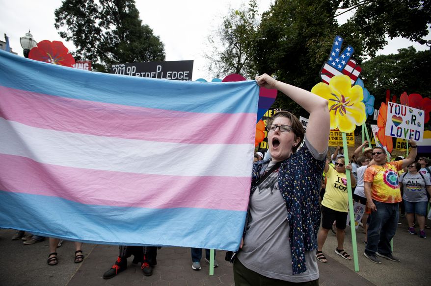 A supporter for the transgender community holds up a flag in front of counter-protesters at the city's Gay Pride Festival in Atlanta on Oct. 12, 2019. A federal judge in Atlanta has blocked Georgia from enforcing part of a new law that restricts doctors from prescribing hormone therapy to transgender people under the age of 18. Judge Sarah Geraghty granted a preliminary injunction on Sunday, Aug. 20. (AP Photo/Robin Rayne, file)
