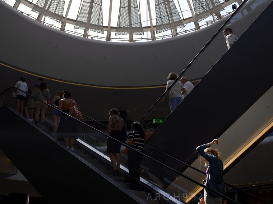 People take the escalator in a shopping mall during a heat wave in Lyon, central France, Wednesday, Aug. 23, 2023. A mall in Southern California will soon require unaccompanied minors to wear identification cards after a crowd of youths started three brawls at the shopping center during last weekend's National Cinema Day promotion. (AP Photo/Laurent Cipriani)