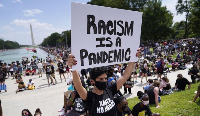 Priscilla Duerrero holds a sign reading &quot;Racism Is A Pandemic&quot; during the March on Washington, Friday, Aug. 28, 2020, at the Lincoln Memorial in Washington, on the 57th anniversary of the Rev. Martin Luther King Jr.&#x27;s &quot;I Have A Dream&quot; speech. (AP Photo/Julio Cortez, File)