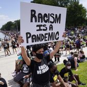 Priscilla Duerrero holds a sign reading &quot;Racism Is A Pandemic&quot; during the March on Washington, Friday, Aug. 28, 2020, at the Lincoln Memorial in Washington, on the 57th anniversary of the Rev. Martin Luther King Jr.&#x27;s &quot;I Have A Dream&quot; speech. (AP Photo/Julio Cortez, File)