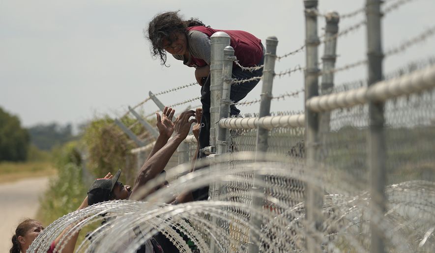 Migrants who crossed the Rio Grande from Mexico into the U.S. climb a fence with barbed wire and concertina wire, Monday, Aug. 21, 2023, in Eagle Pass, Texas. (AP Photo/Eric Gay)