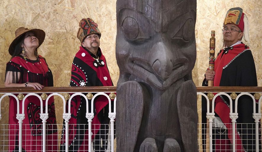 Earl Stephens, who has the Nisga'a cultural name Chief Ni'is Joohl, centre left, with Pamela Brown, left and another member of the delegation from the Nisga'a nation pose beside the 11-metre tall memorial pole, during a visit to the National Museum of Scotland, ahead of its return to what is now British Columbia, in Edinburgh, Monday, Aug. 28, 2023. Members of a Canadian First Nation held a spiritual ceremony on Monday at a Scottish museum to begin the homeward journey of a totem pole stolen almost a century ago. (Andrew Milligan/PA via AP)