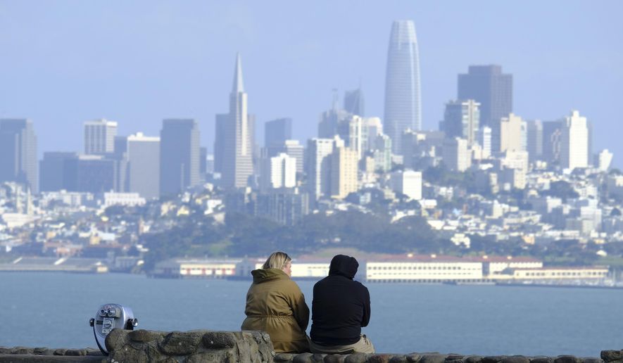 A couple sits at a vista point with the San Francisco skyline in the background on March 27, 2020, in Sausalito, Calif. California, a state known for its ambitious climate policies, could soon adopt new laws reducing emissions from buildings, easing the burden on taxpayers to clean up abandoned oil and gas wells, and requiring the most sweeping emissions reporting mandates for large companies in the nation. (AP Photo/Eric Risberg)