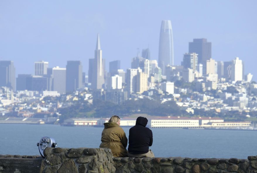 A couple sits at a vista point with the San Francisco skyline in the background on March 27, 2020, in Sausalito, Calif. California, a state known for its ambitious climate policies, could soon adopt new laws reducing emissions from buildings, easing the burden on taxpayers to clean up abandoned oil and gas wells, and requiring the most sweeping emissions reporting mandates for large companies in the nation. (AP Photo/Eric Risberg)