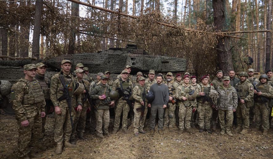 In this photo provided by the Ukrainian Presidential Press Office, Ukrainian President Volodymyr Zelenskyy, center, poses for photo with the Ukrainian soldiers in front of a Leopard 2 tank on the front line in the Kharkiv region, Ukraine, Tuesday, Oct. 3, 2023. (Ukrainian Presidential Press Office via AP)