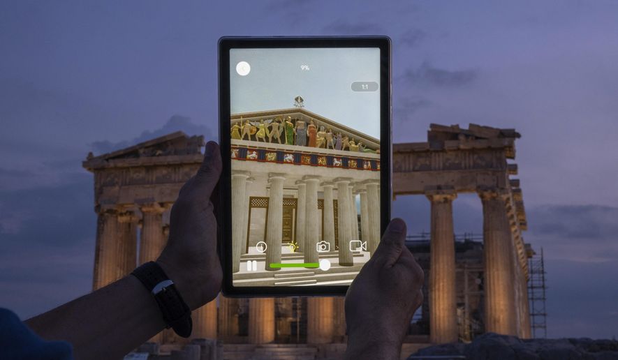 A man holds up a tablet showing a digitally overlayed virtual reconstruction of the ancient Parthenon temple, at the Acropolis Hill in Athens, Greece on Tuesday, June 13, 2023. Greece has become a late but enthusiastic convert to new technology as a way of displaying its famous archaeological monuments and deepening visitors' knowledge of ancient history. The latest virtual tour on offer is provided by a mobile app that uses Augmented Reality to produce digital overlays that show visitors at the Acropolis how the site and its sculptures looked 2,500 ago. (AP Photo/Petros Giannakouris)