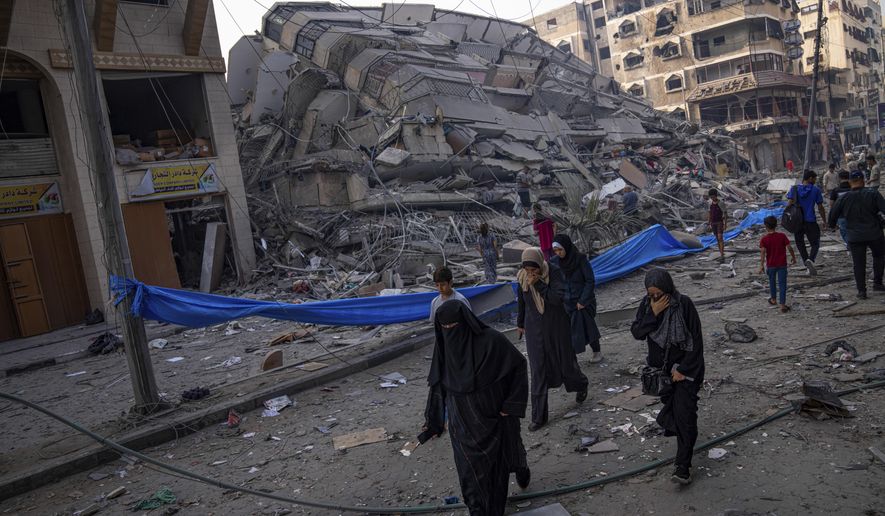 Palestinians walk by the rubble of a building after it was struck by an Israeli airstrike, in Gaza City, Sunday, Oct. 8, 2023. The militant Hamas rulers of the Gaza Strip carried out an unprecedented, multi-front attack on Israel at daybreak Saturday, firing thousands of rockets as dozens of Hamas fighters infiltrated the heavily fortified border in several locations by air, land, and sea, killing hundreds and taking captives. Palestinian health officials reported scores of deaths from Israeli airstrikes in Gaza. (AP Photo/Fatima Shbair)