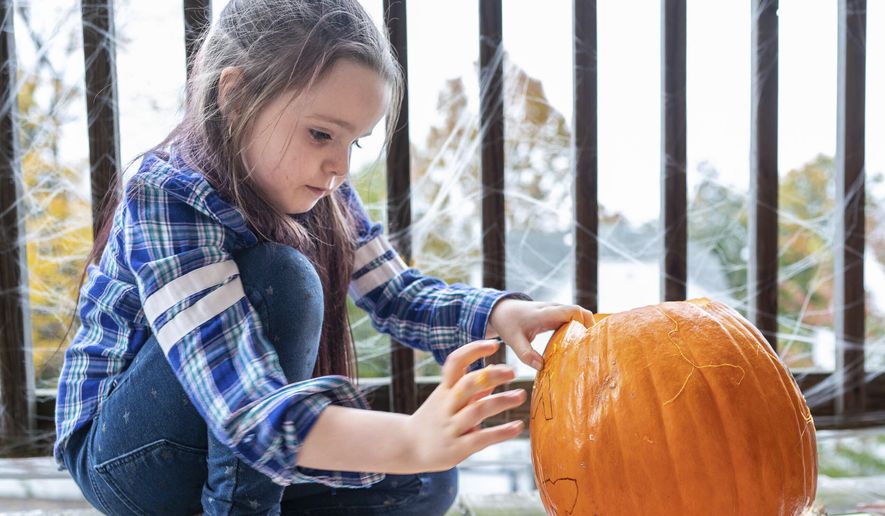 Lola Michaud, 7, pushes out the eyebrow on her carved pumpkin on her front porch, Friday, Oct. 20, 2023 in Auburn, Maine. She and her sister, Eevee, carve several pumpkins every Halloween season. (Andree Kehn/Sun Journal via AP)