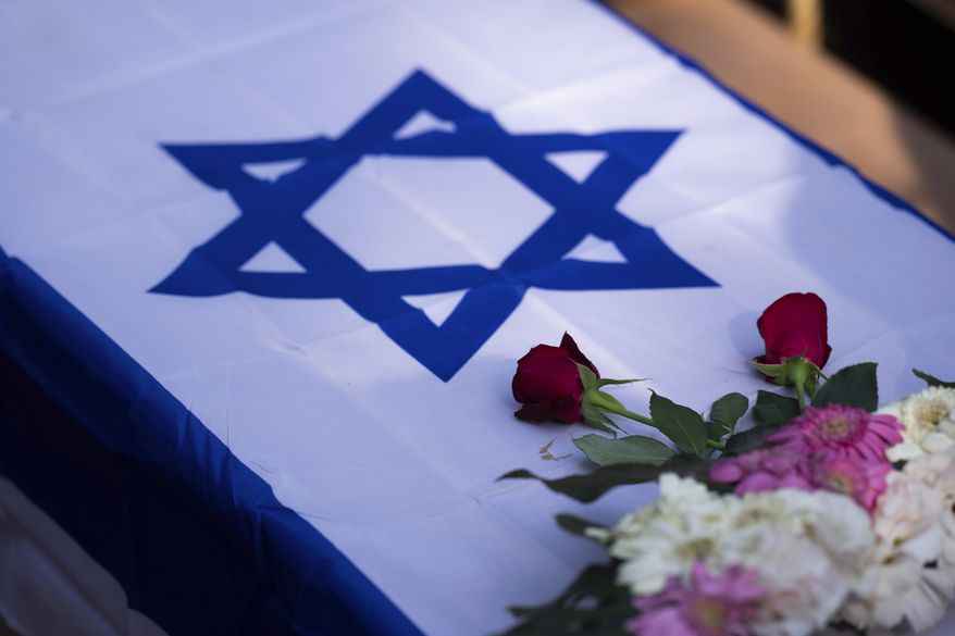 Flowers stand on a coffin draped with the Israeli flag during the funeral of Dana Bachar and her son Carmel, at Gan Shlomo cemetery, central Israel, Tuesday, Oct. 24, 2023. Carmel Bachar, a 15-year-old, and his mother Dana lived in kibbutz Be'eri, a small community with a little more than 1,000 people, that was one of more than 20 towns and villages ambushed on Oct. 7 as part of a surprise attack by Hamas militants against Israel where dozens were killed.(AP Photo/Petros Giannakouris)