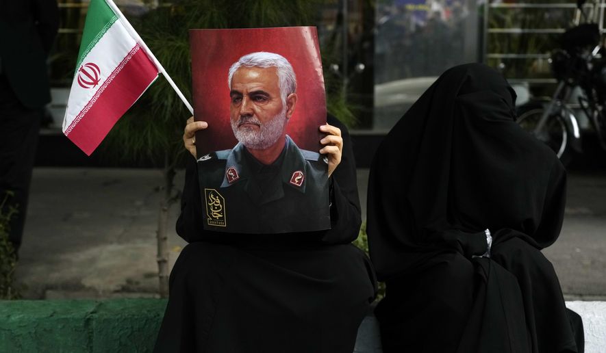A demonstrator holds a poster of the late Iranian Revolutionary Guard Gen. Qassem Soleimani, who was killed in a U.S. drone attack in 2020, and an Iranian flag during a rally in front of the former U.S. Embassy in Tehran, Iran, marking 44th anniversary of the seizure of the embassy by militant Iranian students, Saturday, Nov. 4, 2023. (AP Photo/Vahid Salemi)