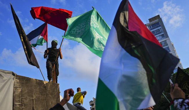 A Palestinian man holds a Palestinian and Hamas flags as others chant slogans against Britain, taking part in a protest near of the British Embassy in Beirut, in solidarity with the Palestinian people in Gaza, Tuesday, Nov. 14, 2023. (AP Photo/Hassan Ammar)
