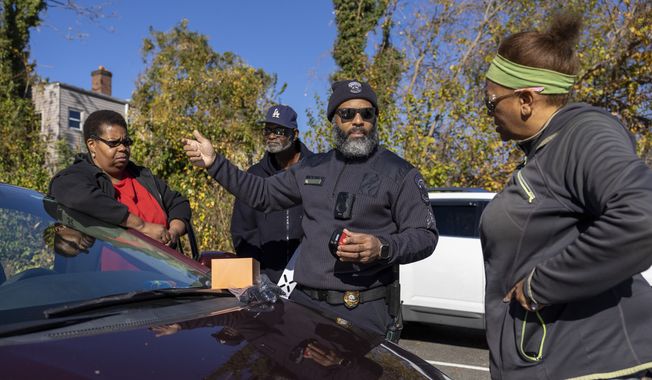 Sgt. Jason Godfrey explains to Grace Djemba, a delivery driver, and Bernard, who did not give his last name, and Terezia Williams, both of whom are Uber drivers, the best place to attach their dashboard cameras during an event where car cameras were distributed to drivers in an effort to combat a rise in crime, hosted in the parking lot of Robert F. Kennedy Stadium in Washington, Tuesday, Nov. 14, 2023. (AP Photo/Amanda Andrade-Rhoades)
