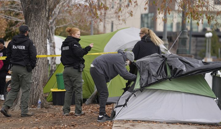 A person collects items from a tent as Denver Parks Department rangers string police tape during a city-sponsored sweep of an encampment overlooking the city skyline on Diamond Hill on Wednesday, Nov. 1, 2023, in Denver. The sweep was just one of several staged in various locations across the Mile High City. (AP Photo/David Zalubowski)