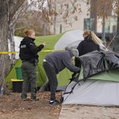 A person collects items from a tent as Denver Parks Department rangers string police tape during a city-sponsored sweep of an encampment overlooking the city skyline on Diamond Hill on Wednesday, Nov. 1, 2023, in Denver. The sweep was just one of several staged in various locations across the Mile High City. (AP Photo/David Zalubowski)