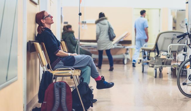 Patient sitting in hospital ward hallway waiting room with iv. File photo credit: JGA via Shutterstock.
