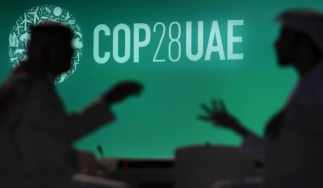 People are silhouetted against a logo for the COP28 U.N. Climate Summit, Wednesday, Nov. 29, 2023, in Dubai, United Arab Emirates. (AP Photo/Rafiq Maqbool)