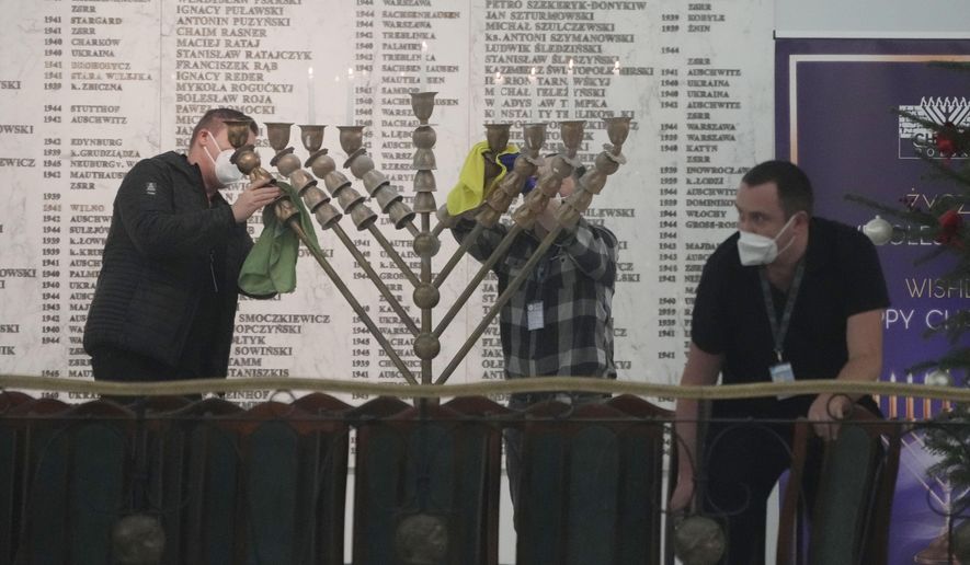 Workers in the Polish parliament clean up a menorah after a far-right lawmaker grabbed a fire extinguisher and put out a candle, disturbing a celebration of the Jewish holiday of Channukah, in Warsaw, Poland, on Tuesday Dec. 12, 2023. (AP Photo/Czarek Sokolowski)