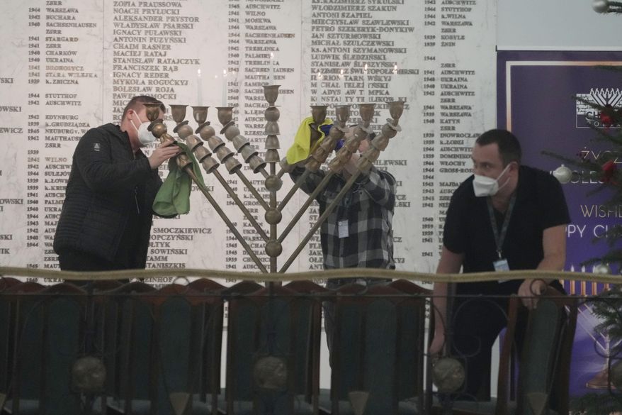 Workers in the Polish parliament clean up a menorah after a far-right lawmaker grabbed a fire extinguisher and put out a candle, disturbing a celebration of the Jewish holiday of Channukah, in Warsaw, Poland, on Tuesday Dec. 12, 2023. (AP Photo/Czarek Sokolowski)