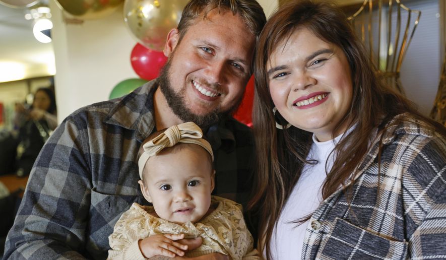 Alan Shurtleff, left, Morgan Shurtleff, right, and their daughter, 1-year-old Cora Dibert, pose for a photo at The Bridge Church, Saturday, Dec. 2, 2023, in Mustang, Okla. When Cora went for a routine blood test in October, the toddler brought along her favorite new snack: a squeeze pouch of WanaBana cinnamon-flavored apple puree. Within a week, the family got an alarming call. The test showed that the 1-year-old had lead poisoning, with nearly four times as much lead as the level that raises concern. (AP Photo/Nate Billings)