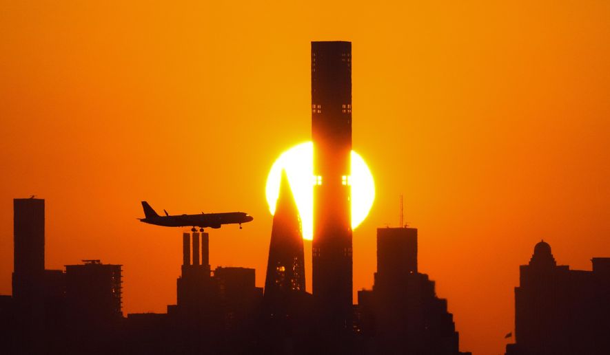 The sun sets behind the Manhattan skyline as a plane approaches LaGuardia Airport on Sept. 6, 2023, in New York. Holiday travel is kicking off on highways, trains, and airports this week. (AP Photo/Frank Franklin II, File)