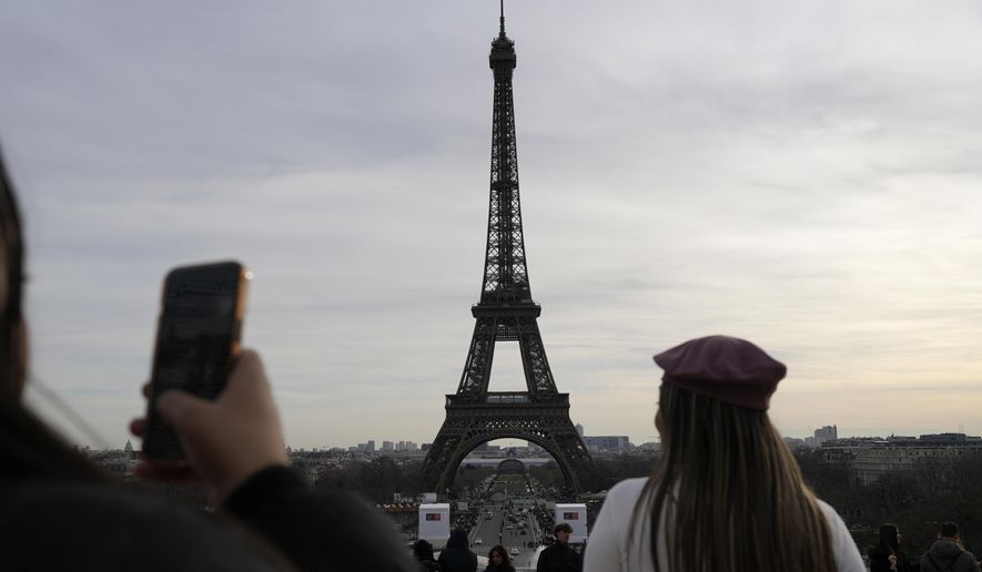 Tourists watch the Eiffel Tower, Wednesday, Dec. 27, 2023 in Paris. The Eiffel Tower was shut down to visitors Wednesday because of a strike over contract negotiations, the day the Paris monument marks 100 years since the death of its creator, Gustave Eiffel. Tourists can still access the glass-enclosed esplanade beneath the tower, but access to the 300-meter (984-foot) landmark itself is closed until further notice, (AP Photo/Lewis Joly)