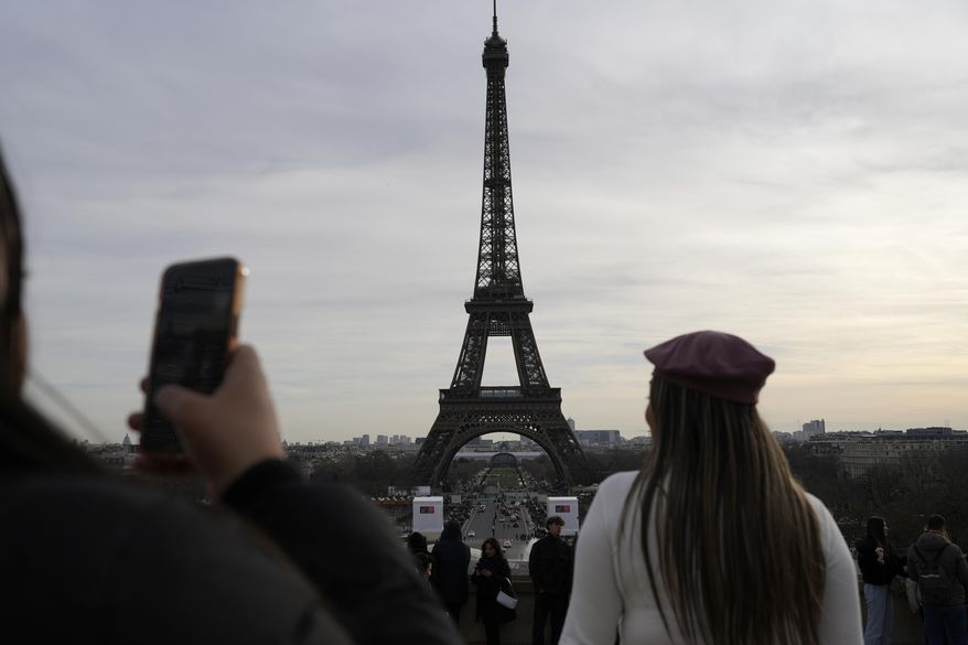 Tourists watch the Eiffel Tower, Wednesday, Dec. 27, 2023 in Paris. The Eiffel Tower was shut down to visitors Wednesday because of a strike over contract negotiations, the day the Paris monument marks 100 years since the death of its creator, Gustave Eiffel. Tourists can still access the glass-enclosed esplanade beneath the tower, but access to the 300-meter (984-foot) landmark itself is closed until further notice, (AP Photo/Lewis Joly)