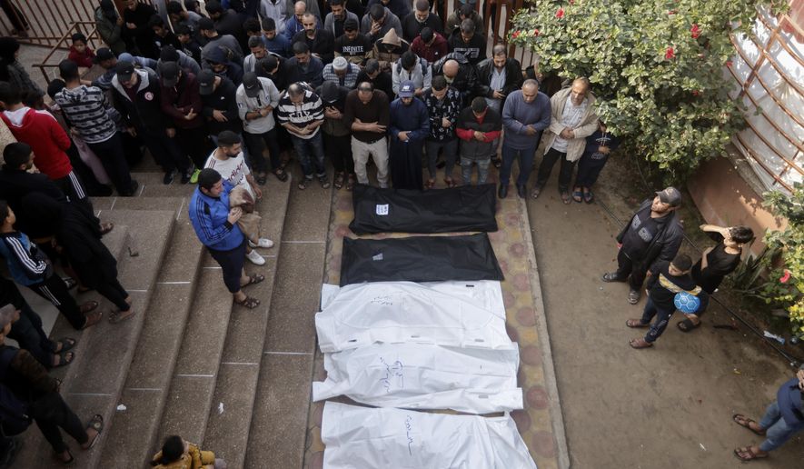 Palestinians pray near the wrapped bodies of relatives killed in the Israeli bombardment of the Gaza Strip, outside a morgue in Khan Younis on Wednesday, Dec. 27, 2023. (AP Photo/Mohammed Dahman)