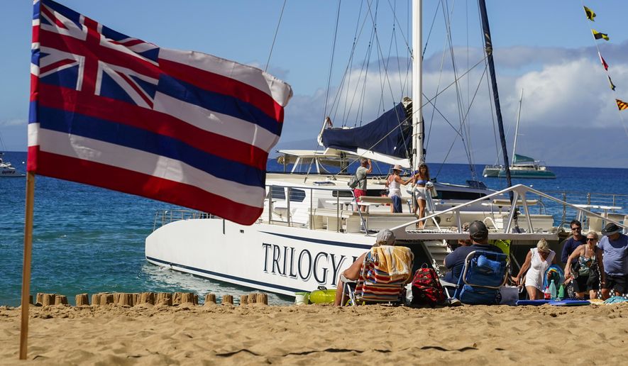 Tourists get off of a Trilogy Excursions boat arriving on Kaanapali Beach in front of a flag of Hawaii planted in the sand, Wednesday, Dec. 6, 2023, in Lahaina, Hawaii. Residents and survivors still dealing with the aftermath of the August wildfires in Lahaina have mixed feelings as tourists begin to return to the west side of Maui. (AP Photo/Lindsey Wasson)