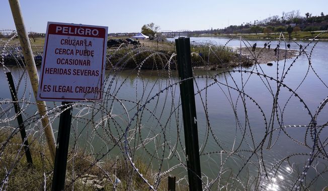 Migrants cross the Rio Grande into the U.S. from Mexico behind Concertina wire and a sign warning that it&#x27;s dangerous and illegal to cross, Wednesday, Jan. 3, 2024, in Eagle Pass, Texas. According to U.S. officials, a Mexican enforcement surge has contributed to a sharp drop in illegal entries to the U.S. in recent weeks. (AP Photo/Eric Gay)