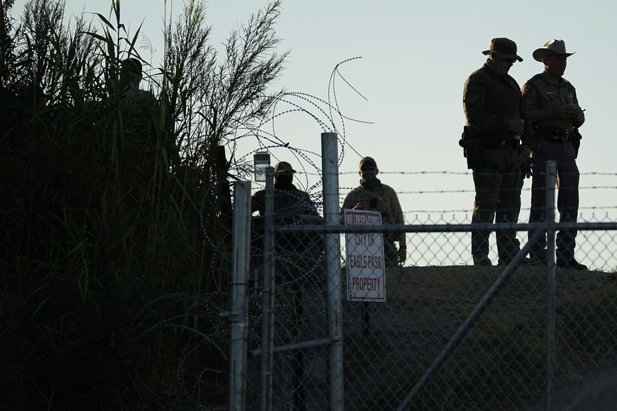Texas troopers stand near a "No Trespassing" sign and concertina wire along the banks of the Rio Grande at Shelby Park, Aug. 1, 2023, in Eagle Pass, Texas. The mayor of Eagle Pass, a Texas border city that's at the center of Republican Gov. Greg Abbott's aggressive measures to curb migrant crossings, accused the state Thursday, Jan. 11, 2024, of a new escalation, saying state troopers closed Shelby Park without asking permission. (AP Photo/Eric Gay, File)