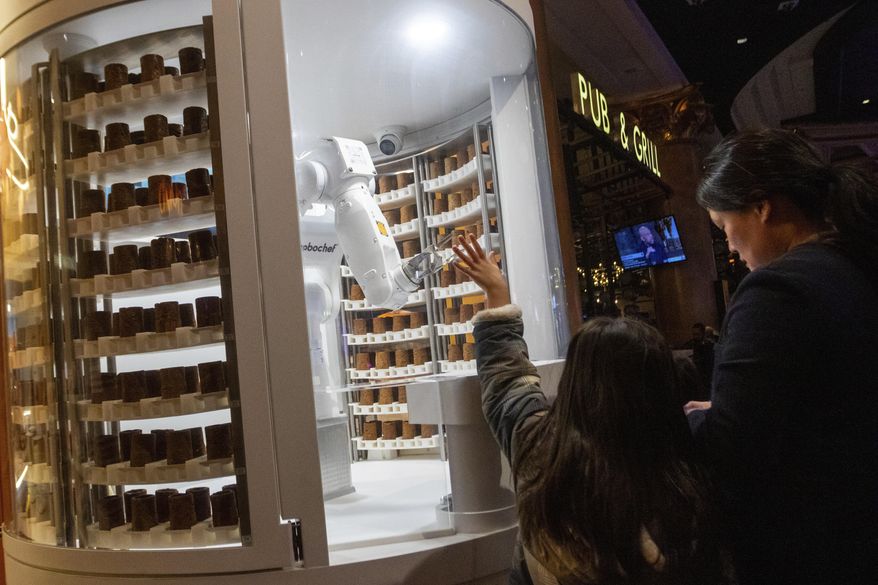 A child waves to a robot dessert booth at Caesars Palace, Thursday, Jan. 11, 2024, in Las Vegas. Chef-like robots and barista bots caused a stir at the annual CES technology trade show in Las Vegas, putting a spotlight on casino union workers' fears that jobs could be at risk in the age of artificial intelligence. (AP Photo/ Ty ONeil) **FILE**