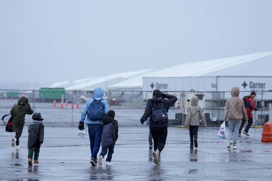 Immigrants run in the rain towards the tents at migrant housing location at Floyd Bennett Field, Tuesday, Jan. 9, 2024. (AP Photo/Mary Altaffer)