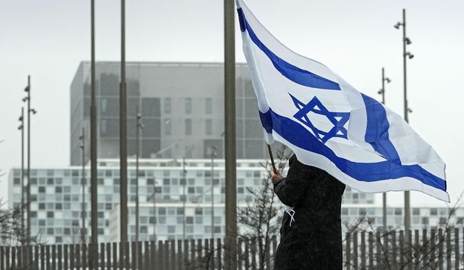 A woman holds an Israeli flag in front of International Criminal Court at The Hague, Netherlands, before a demonstration of representatives of families of hostages from the Oct. 7 cross-border attack by Hamas on Israel, Wednesday, Feb. 14, 2024. The Hostages Families Forum together with the Raoul Wallenberg Center for Human Rights want to submit a comprehensive complaint to the International Criminal Court on behalf of released hostages and families of hostages, including the issuance of arrest warrants for Hamas leaders on war crimes allegations including taking hostages, enforced disappearances, sexual violence and torture. (AP Photo/Martin Meissner)