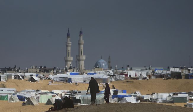 Palestinians displaced by the Israeli ground offensive on the Gaza Strip walk at the makeshift tent camp in Rafah, Gaza Strip, Sunday, Feb. 18, 2024. (AP Photo/Mohammed Dahman)