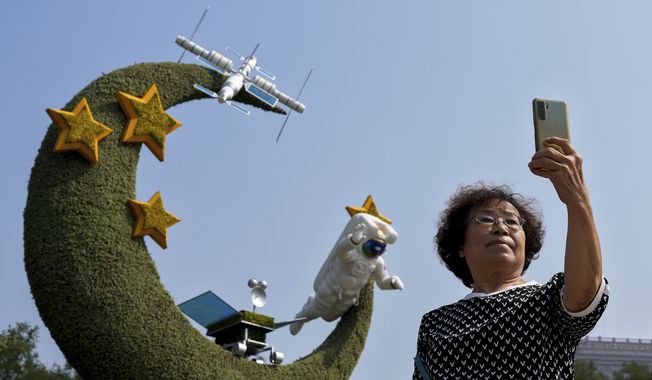A woman takes a souvenir photo with a floral decoration featuring China&#x27;s space programs celebrating National Day and the 20th party congress in Beijing on Sept. 26, 2022. The U.S. is closely monitoring Chinese activities that potentially threaten American assets in space and is deeply concerned about the rapidly accumulating amount of space debris in low earth orbit, the head of United States military operations in space said Friday, Dec. 9, 2022. (AP Photo/Andy Wong) ** FILE **