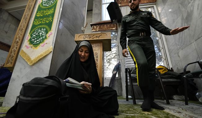 A woman fills out her ballot as a policeman walks past during the parliamentary and Assembly of Experts elections at a polling station in Tehran, Iran, Friday, March 1, 2024. Iran held the country&#x27;s first election since the mass 2022 protests over mandatory hijab laws after the death in police custody of Mahsa Amini, with questions looming over just how many people will turn out at the polls. (AP Photo/Vahid Salemi)