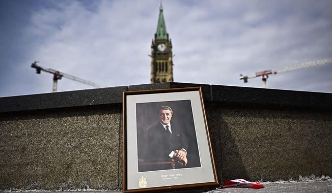 A framed portrait of former Prime Minister Brian Mulroney leans against the Centennial Flame on Parliament Hill as Canadians mourn his death at the age of 84, in Ottawa, Canada on Friday, March 1, 2024. (Justin Tang/The Canadian Press via AP)