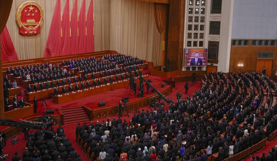 A screen shows Chinese President Xi Jinping as leaders and delegates stand for national anthem during the closing session of the National People's Congress (NPC) at the Great Hall of the People in Beijing, Monday, March 11, 2024. (AP Photo/Andy Wong)