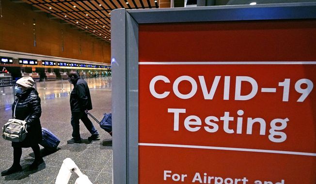Travelers pass a sign near a COVID-19 testing site in Terminal E at Logan Airport, on Dec. 21, 2021, in Boston. The nation’s top public health agency is expanding a program that tests international travelers for COVID-19 and other infectious diseases. The Centers for Disease Control and Prevention currently operates a program at six U.S. airports that asks passengers from inbound international flights to agree to nose swabs and answer questions about their travel. (AP Photo/Charles Krupa, File)