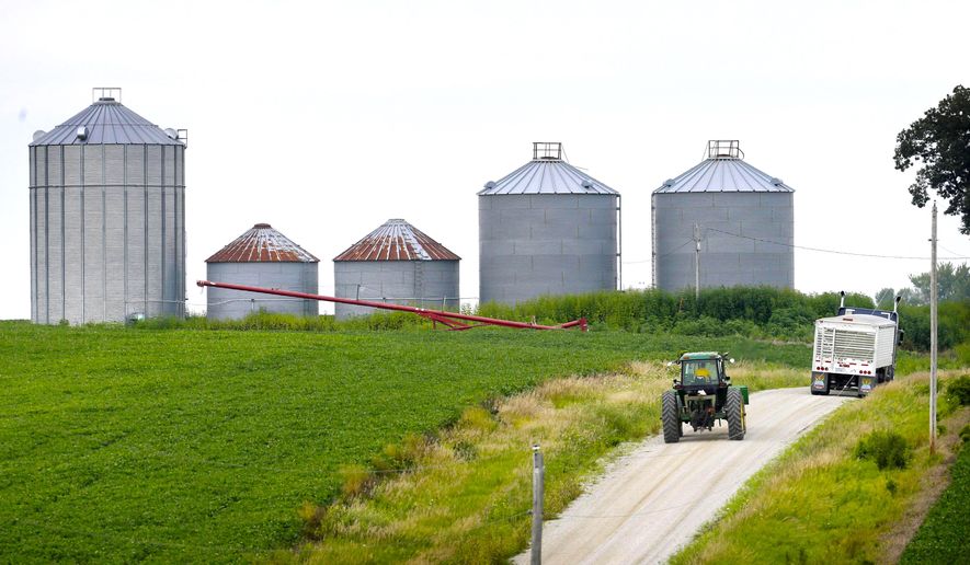 A farmer drives his tractor past a soybean field toward grain storage bins near Ladora, Iowa. (AP Photo/Charlie Neibergall, File)