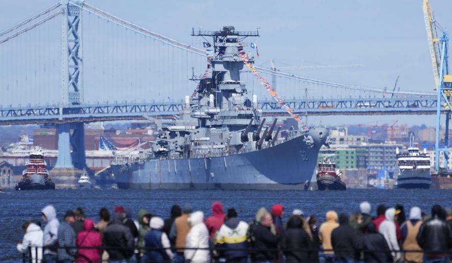 People gather in Gloucester City, N.J., to view the USS New Jersey moved down Delaware River Thursday, March 21, 2024. The retired battleship is initially headed to the Paulsboro Marine Terminal, where it will be balanced to prepare for dry docking, and will then go to the Philadelphia Navy Yard. (AP Photo/Matt Rourke)