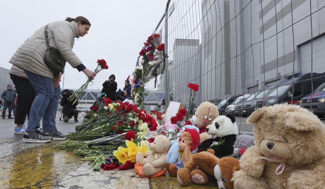 A woman places flowers by the fence next to the Crocus City Hall, on the western edge of Moscow, Russia, Saturday, March 23, 2024, following an attack Friday, for which the Islamic State group claimed responsibility. Russian officials say more than 90 people have been killed by assailants who burst into a concert hall and sprayed the crowd with gunfire. (AP Photo/Vitaly Smolnikov)
