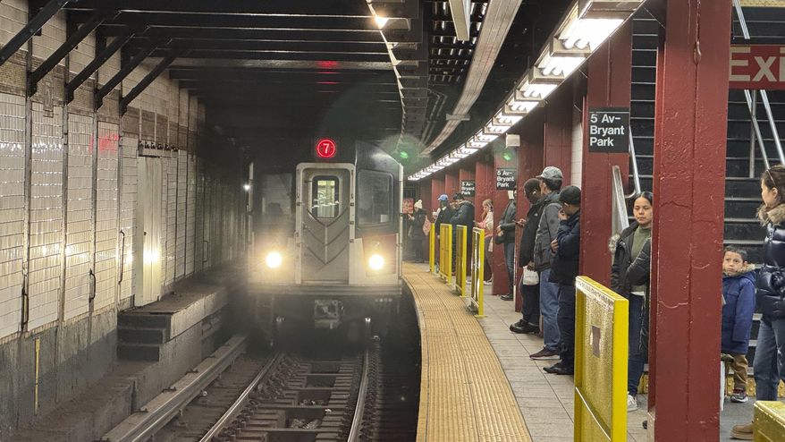 Subway riders stand near yellow barriers on a platform of the 7 train in New York on Tuesday, March 26, 2024. The city is experimenting with barriers to improve safety. (AP Photo/Cedar Attanasio)