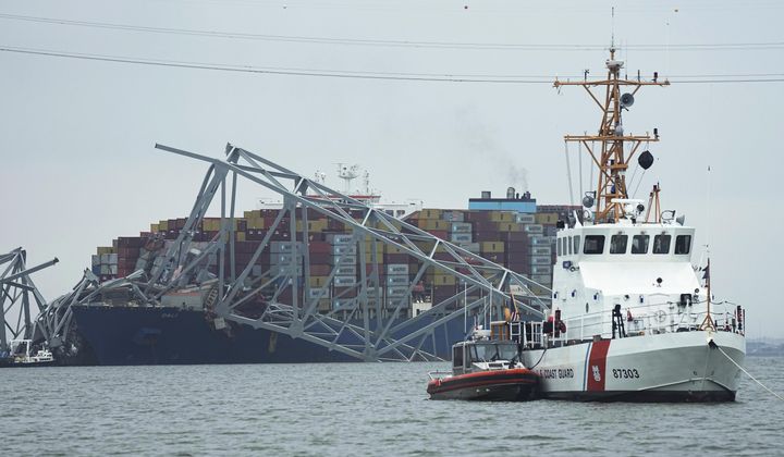 A Coast Guard cutter patrols in front of a cargo ship stuck under part of the structure of the Francis Scott Key Bridge on on Wednesday March 27, 2024, one day after the ship hit the bridge in Baltimore, Md., causing it to collapse. (AP Photo/Steve Helber)