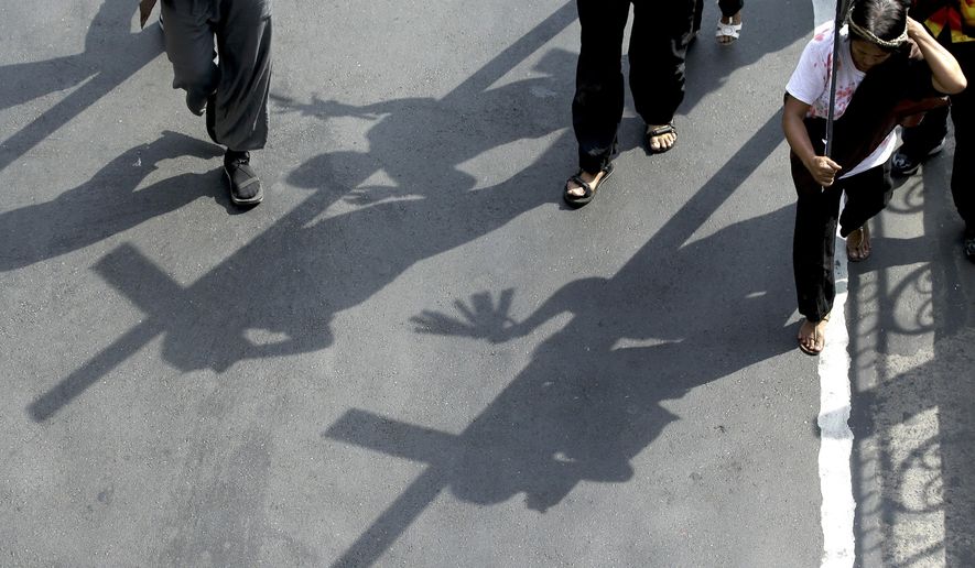 FILE - Shadows of protesters carrying wooden crosses are reflected on the street as they reenact the sufferings of Jesus Christ during a rally on holy week in Manila, Philippines, on March 27, 2018. A Filipino villager plans to be nailed to a wooden cross for the 35th time to reenact Jesus Christ’s suffering in a brutal Good Friday tradition he said he would devote to pray for peace in Ukraine, Gaza and the disputed South China Sea. (AP Photo/Aaron Favila, File)