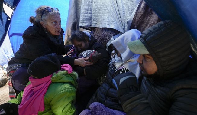 Medical volunteer Karen Parker, left, touches a 2-year-old child with a fever as she talks to a family of asylum-seeking migrants as they wait to be processed in a makeshift, mountainous campsite after crossing the border with Mexico, Feb. 2, 2024, near Jacumba Hot Springs, Calif. A federal judge on Friday, March 29, sharply questioned the Biden administration&#x27;s position that it bears no responsibility for housing and feeding migrant children while they wait in makeshift camps along the U.S-Mexico border. (AP Photo/Gregory Bull, File)